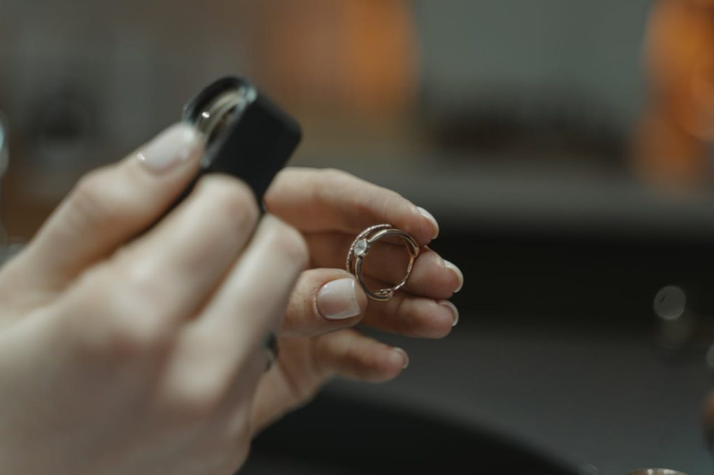 a-person-holding-a-diamond-ring-6263113 Close-up of a jewelers hands holding a diamond ring and magnifying glass.